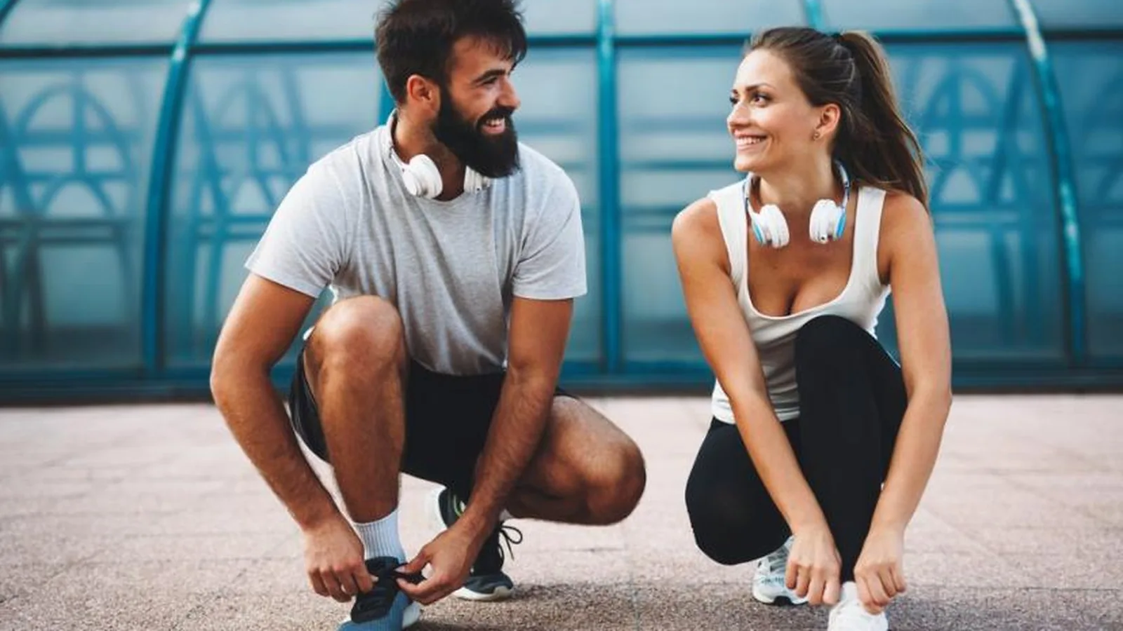 Deux coureurs accroupis côte à côte, souriants, qui lacent leurs chaussures avant de partir courir